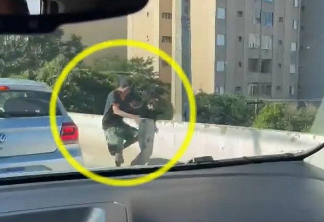 Homem correndo e pulando mureta ao lado de carros, no meio do trânsito, sendo flagrado de dentro do carro