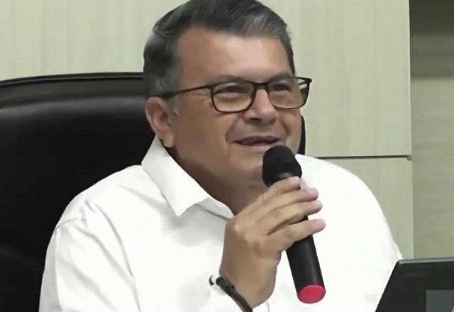 Homem de cabelos grisalhos, segurando microfone e rindo durante discurso