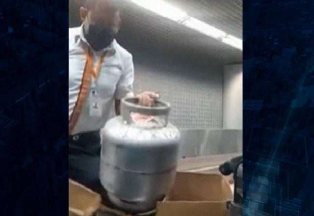 Homem de camisa branca segurando botijão de gás em área reservada de aeroporto