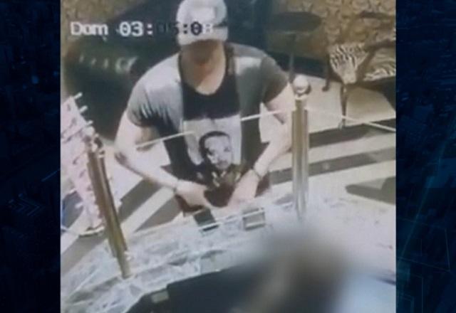 Homem de camiseta preta em recepção de estabelecimento comercial, flagrado por camera de segurança