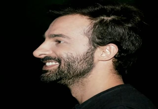 Homem de camiseta preta sorri de perfil