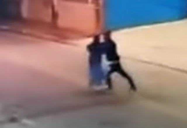 Homem de capuz empurrando mulher com de saia azul para uma calçada