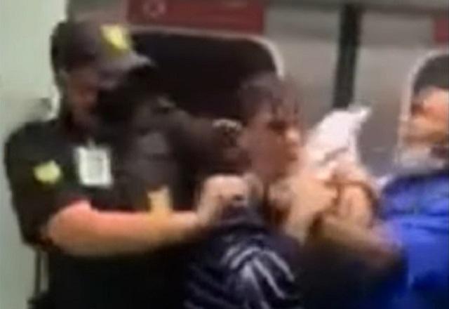 Homem de farda preta, segurança, segura outro homem durante briga em vagão de trem