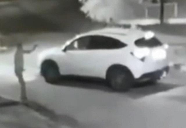 Homem de pé, armado, aponta arma para veículo branco roubado em rua do RJ