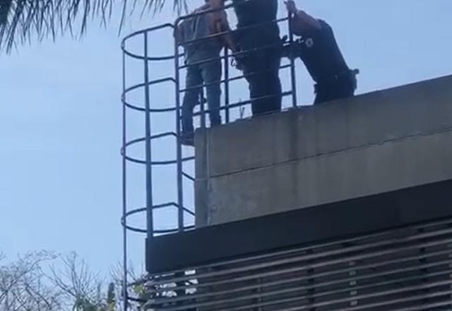 Homem em cima de um telhado cercado por dois guardas civis municipais