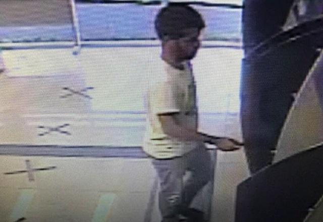 Homem em pé, parado em frente a caixa eletrônico de banco, flagrado do alto por câmera de segurança