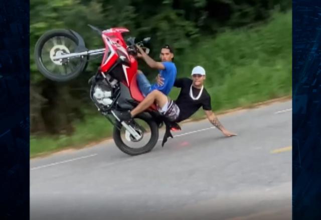 Homem empinando moto e garupa com a mão no asfalto