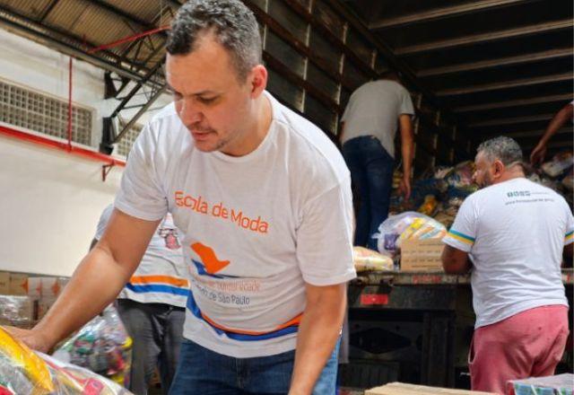 Homem manuseia caixas embaladas de doações, com outros homens ao fundo no interior de um caminhão aberto com mais produtos embalados