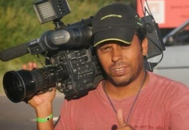 Homem negro, de boné, empunhando câmera nos ombros