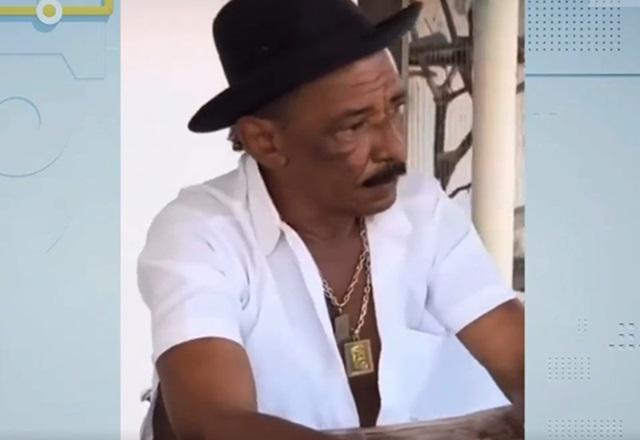 Homem negro de chapéu preto e camisa branca, conversando em mesa