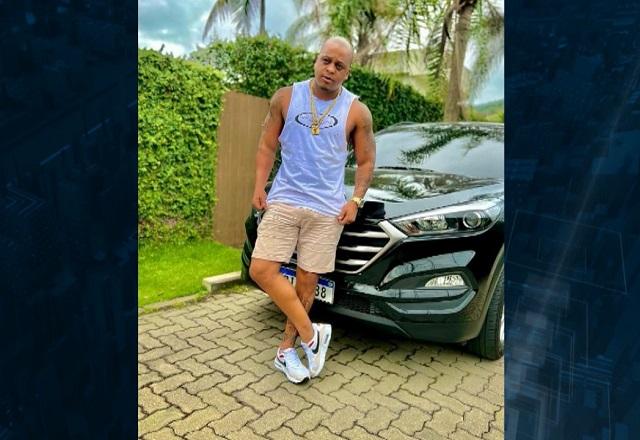 Homem negro e careca, de pé, em frente a carro importado em área verde