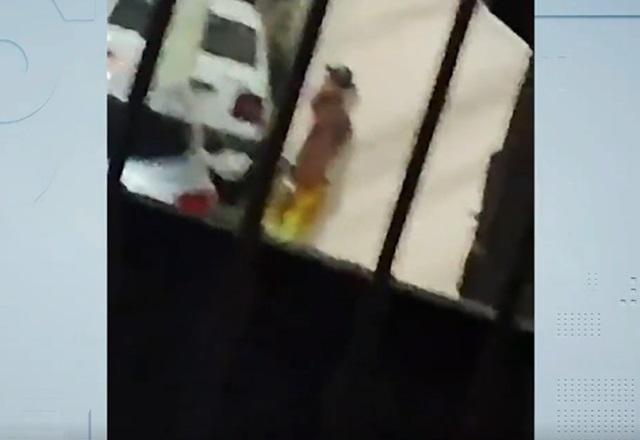 Homem negro sem camiseta se escondendo atrás de muro, em rua, durante a noite