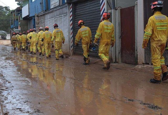 Homens paramentados de amarelo andam em uma terra úmida próximo a estabelecimentos fechados