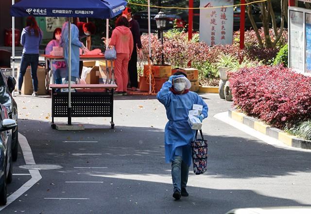 Idosa com máscara e roupa de proteção anda por bairro de Xangai