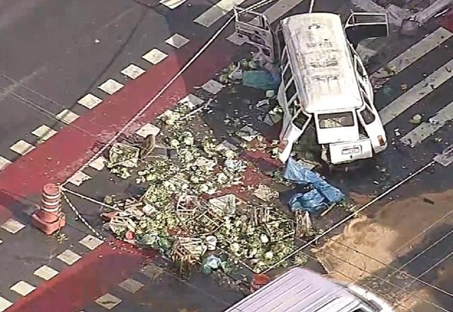 Imagem aérea de veículo kombi destruída após acidente, com verduras e legumes espalhados por avenida