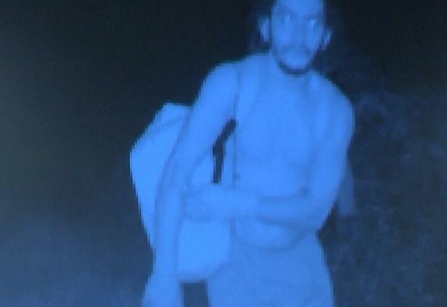 Imagem azulada, capturada por câmera de monitoramento, de homem branco segurando mochila