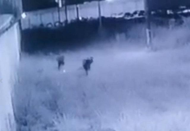 Imagem de camera de segurança em preto e branco com dois suspeitos correndo
