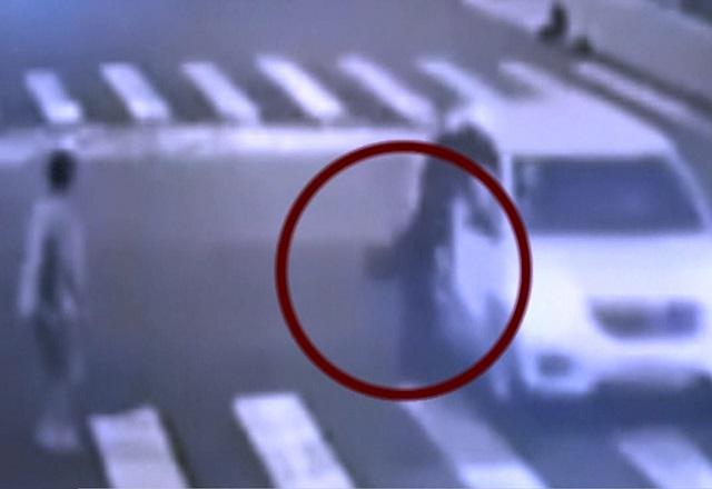 Imagem de câmera de segurança em preto e branco mostra cachorro pulando de janela de carro em movimento e indo em direção à mulher