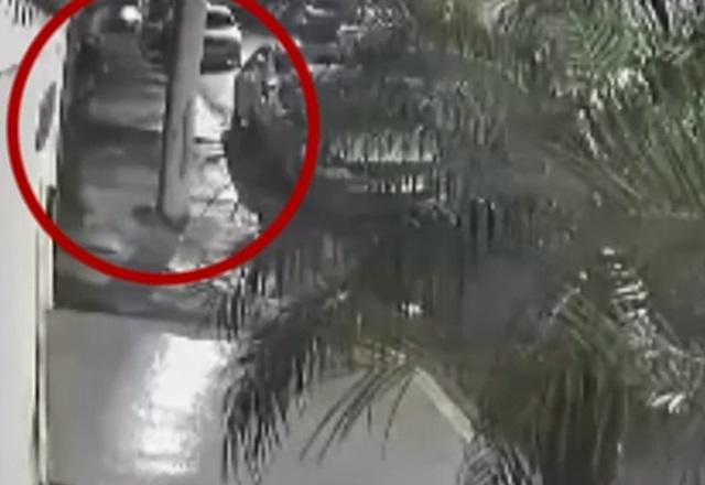 Imagem de câmera de segurança mostrando rua e, em destaque e circulado de vermelho, homem disparando arma de fogo