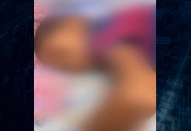 Imagem desfocada para não identificar menor de idade, uma criança negra, deitada na cama de barriga para baixo, se apoiando com o braço