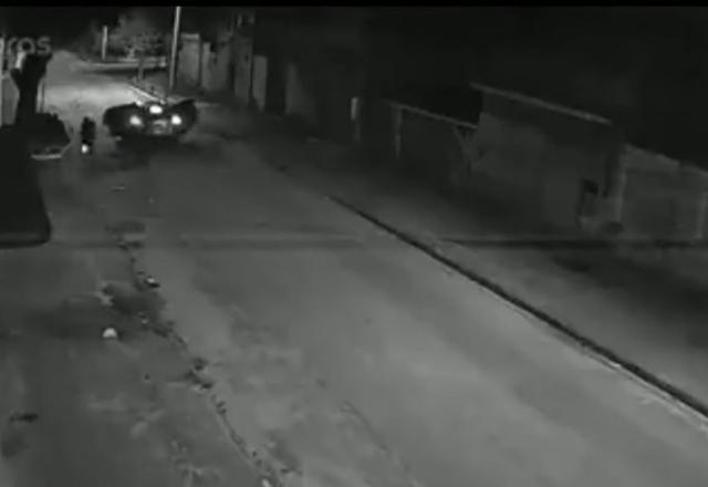 Imagens de segurança que captam a uma certa distância um carro no meio da rua, enquanto todos os ocupantes estão fora atirando contra um homem que entrava no carro estacionado.