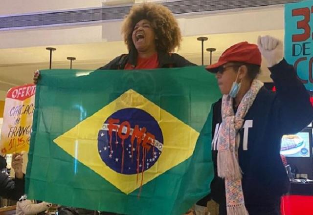 Integrante do MTST segura bandeira do Brasil, com a palavra 'fome' escrita em vermelho no centro, durante protesto em shopping (Reprodução/Instagram)