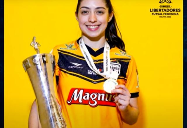 Jogadora uniformizada segurando troféu e medalha
