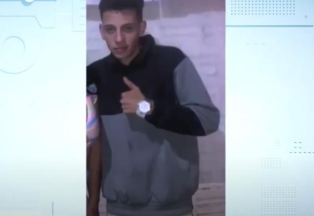 Jovem de blusa cinza e preta acenando para a foto