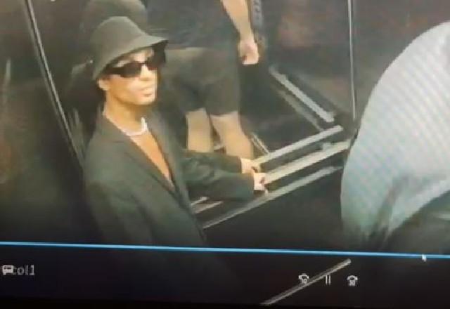 Jovem de óculos escuros, chapéu e blazer preto, dentro de elevador