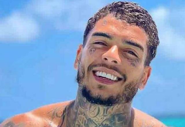 Jovem moreno tatuado sorrindo em uma praia