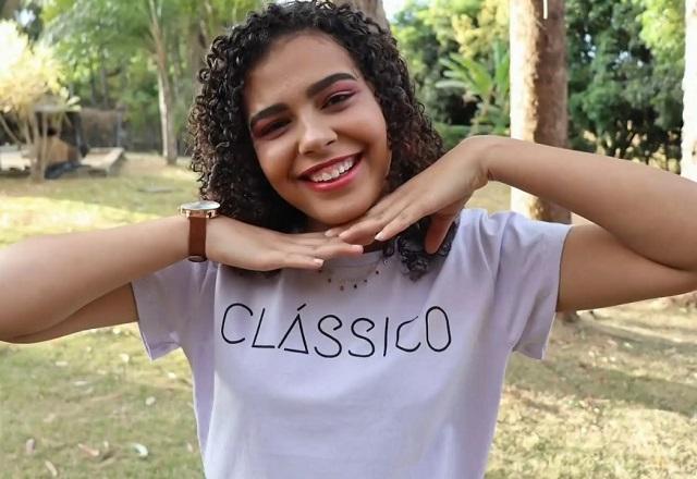 Jovem negra sorrindo, com as mãos unidas embaixo do queixo