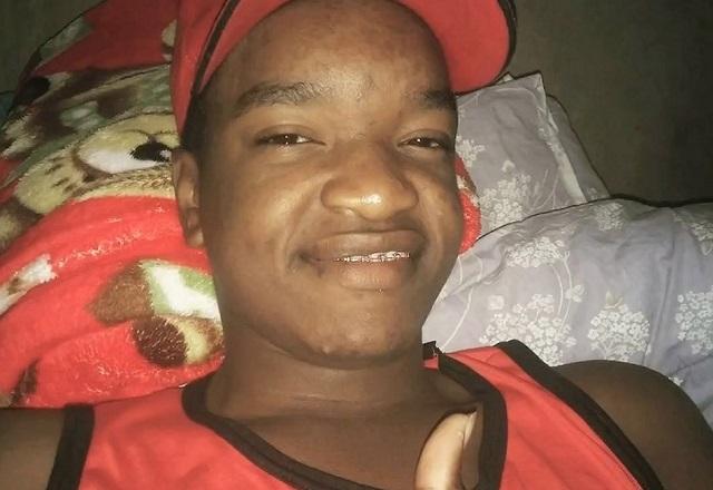 Jovem negro sorrindo, de boné vermelho e regata vermelha, fazendo sinal de joinha com a mão