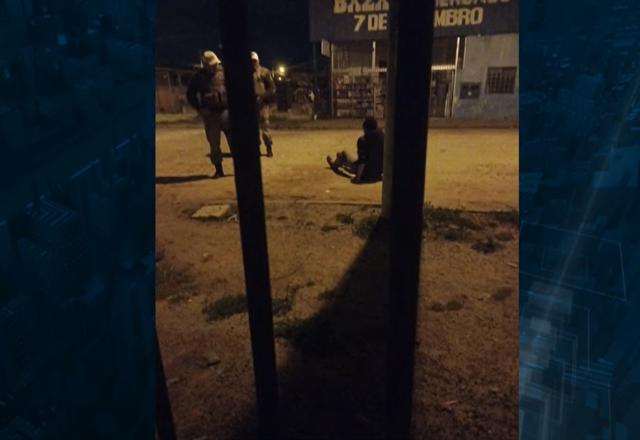 Jovem sentado sendo abordado por policiais