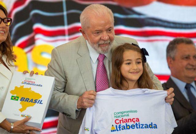 Lula segura uma camiseta com a frase Compromisso Nacional Criança Alfabetizada, com criança ao lado