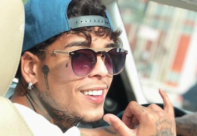 MC Kevin de óculos fazendo sinal hanloose com a mao dentro de um carro
