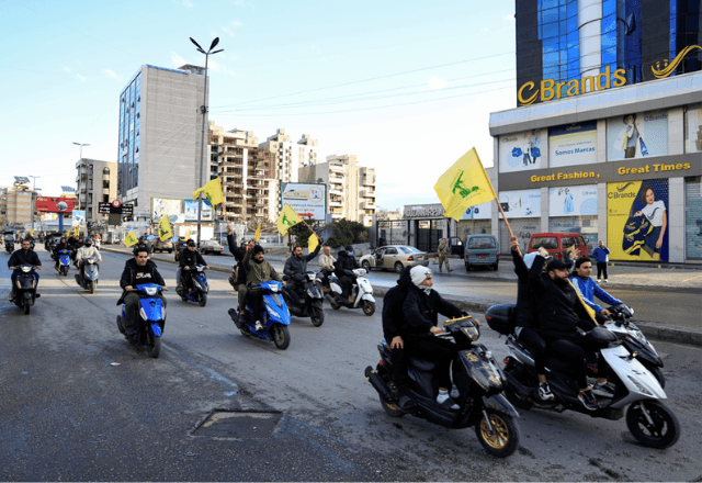 Homens carregam bandeiras do Hezbollah enquanto andam de moto, ao sul de Beirute | Reuters/Thaier Al-Sudani