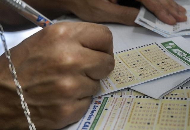 Mão com caneta prateada escrevendo em boleto de aposta de loteria