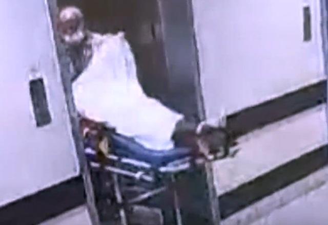 Maqueiro levantando lençol de mulher deitada em maca, dentro de elevador de hospital