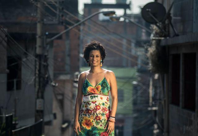 Marielle Franco de vestido, com a favela da Maré ao fundo
