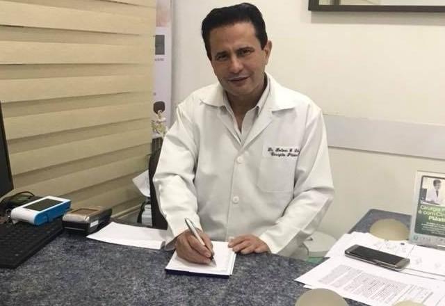 Médico de jaleco branco sentado em consultório com caneta na mão