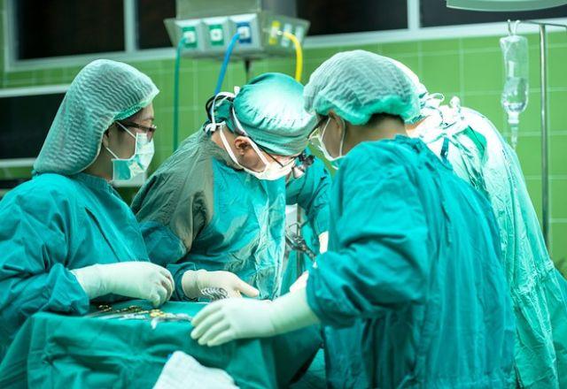 Médicos vestidos de verde estão em um centro cirúrgico fazendo uma operação