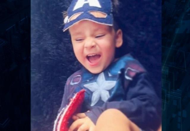 Menino branco, sorrindo para foto e com camiseta azul e desenho de estrela