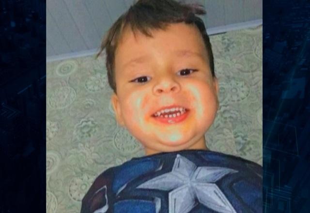 Menino de quatro anos, branco, com camiseta azul e sorrindo para foto