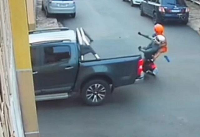 Motociclista a bordo de moto, com garupa, caindo em rua após ser atingido por caminhonete em cruzamento