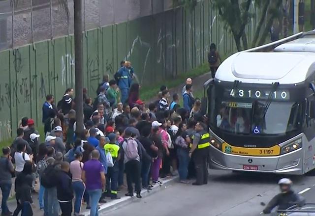 Movimentação de ônibus em avenida, com passageiros esperando para embarcar