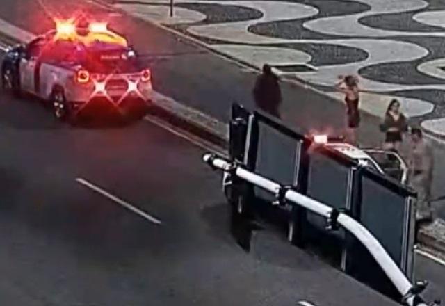 Movimentação de pessoas e viatura policial em avenida de orla de praia, durante a noite