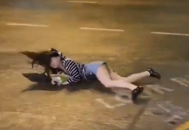 Mulher branca caída no asfalto durante tempestade, à noite