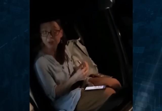 Mulher branca, de óculos, sentada em banco traseiro de passageiro em veículo, enrolando cigarro suspeito