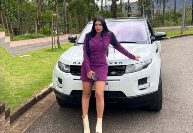 Mulher branca de vestido curto e botas, apoiada na frente de carro branco estacionado em rua