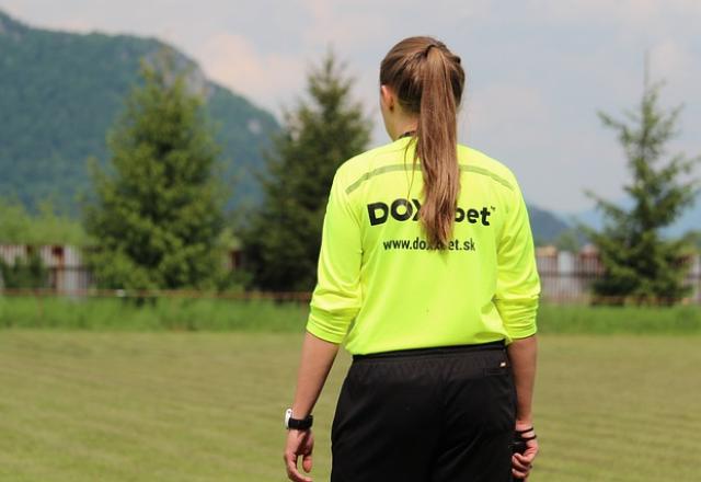 Mulher está de blusa verde e shorts preto em campo de futebol